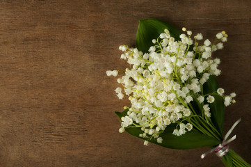 Fototapeta na wymiar Bouquet of tender white lily of the valley on a wooden background.