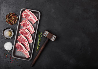Fresh raw butchers lamb beef cutlets in plastic tray with vintage meat hammer on black background.Salt, pepper and oil in steel bowl.Space for text