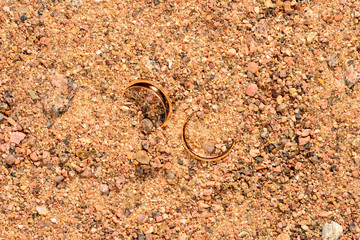 Rejected gold wedding rings buried in sea sand after a divorce.