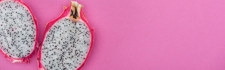 panoramic shot of tropical ripe dragon fruit halves on pink background