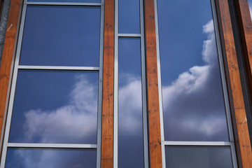Facade with glass and tropical hardwood reflecting vibrant blue sky with clouds 