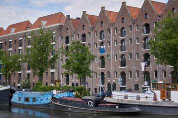 Warehouses with slanted roof in Amsterdam with canal and boats                      