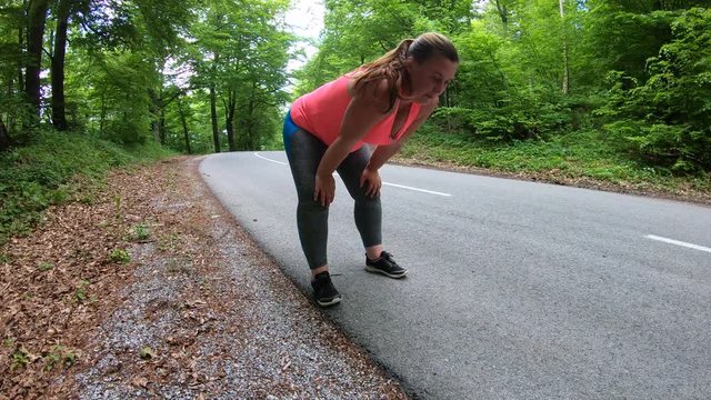 Tracking shot of an overweight woman running on the asphalt road surrounded by lush forest