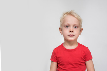 Serious blond boy in a red t-shirt. Space for text. White background