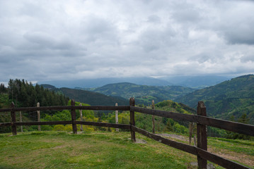 Fototapeta na wymiar Landscape with green meadows and wooden fence with mountains in the background and cloudy sky in Albiztur, Basque Country, Spain, Europe