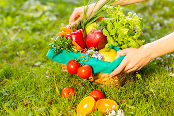 Female hands holding wicker basket with vegetables and fruits, close up