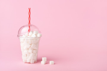 Shake Glass with straw full of sugar cubes on pink background Unhealthy diet concept