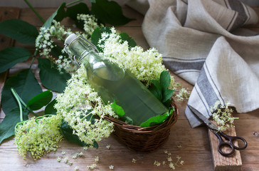 Homemade syrup of elderberry flowers in a glass jar and elder branches on a wooden table Rustic...