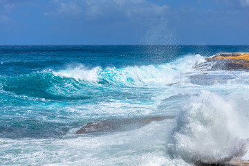 Day storm on a sunny day, turquoise waves of the Mediterranean sea breaking on the rocks.