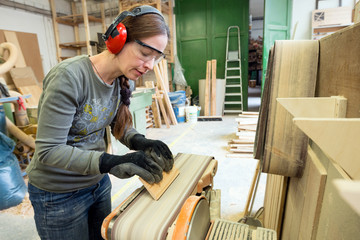 Young woman using a belt sander to sand wooden plank at workshop