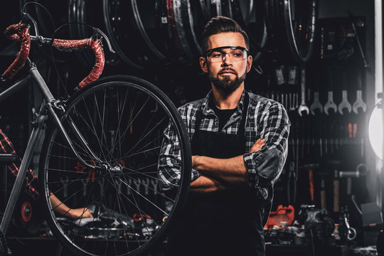 Handsome bearded man in glasses is standing near fixed bicycle at his own workshop.