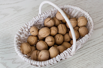 Wicker white small basket with ripe whole walnuts on the table. Top view.