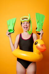 Photo of smiling woman with flippers in hands, swimming mask and with life preserver on empty orange background