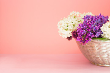 basket with a branch of lilac flowers on a coral pink background. Copy space. Beautiful summer bouquet.