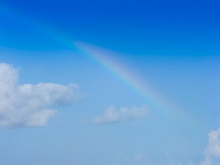 faint rainbow in blue sky with small white clouds - starting and ending rainbow in middle of shot -...