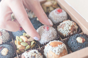 The box with healthy organic sweets with dried fruits, nuts, banana, dates and honey - vegan raw snack. Female hand takes a vegan candy.