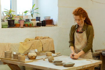 Concentrated long-haired ginger girl intensely warming fresh clay