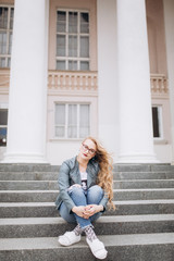 Close up street urban portrait of young fashion stylish pretty blondie woman in fashion jeans in glasses sitting outdoors in the street . Beauty, student, freedom concept