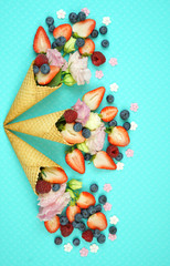 Obraz na płótnie Canvas Summertime flatlay concept with ice cream cones filled with fruit, flowers and candy.