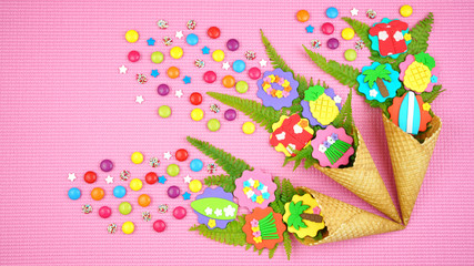 Fototapeta na wymiar Summertime flatlay concept with ice cream cones filled with fruit, flowers and candy.