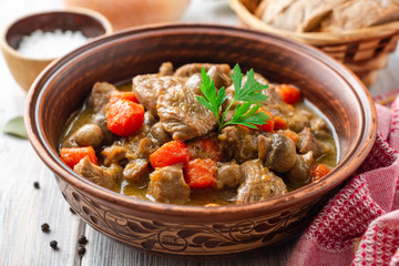 Turkey meat stew with mushrooms and vegetables in ceramic bowl on wooden table. Selective focus.