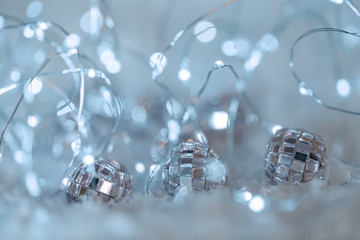 Small decorative balls with a mirror and a luminous garland on a snow. Blurred festive gray background with white bokeh.