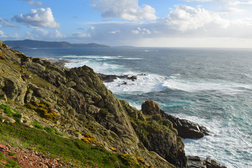 Acantilados y olas rompiendo contra las rocas en un día soleado parcialmente nublado en la costa atlántica de Galícia, España. 