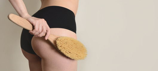 Young woman holding massage brush in her hand, crop on booty
