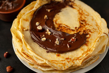 Pancakes with chocolate paste and hazelnuts, on a white plate on a background of concrete, slate