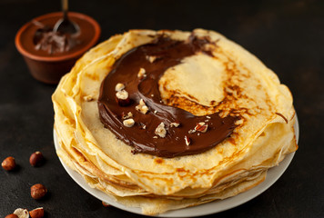 Pancakes with chocolate paste and hazelnuts, on a white plate on a background of concrete, slate