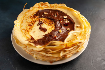 Pancakes with chocolate paste and hazelnuts, on a white plate on a background of concrete, slate
