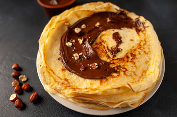 Pancakes with chocolate paste and hazelnuts, on a white plate on a background of concrete, slate