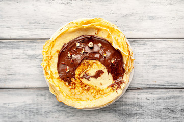 Pancakes with chocolate spread and hazelnuts,  on a white plate on a wood background
