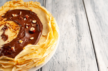 Pancakes with chocolate spread and hazelnuts,  on a white plate on a wood background