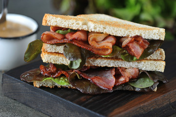 Sandwich with bacon and oaklif lettuce on a dark wooden board. Dark background. Close-up. Macro shooting.