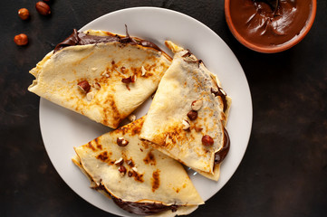 Pancakes with chocolate paste and hazelnuts, on a white plate on a background of concrete, slate