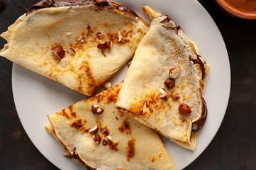 Pancakes with chocolate paste and hazelnuts, on a white plate on a background of concrete, slate