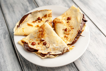 Pancakes with chocolate spread and hazelnuts,  on a white plate on a wood background