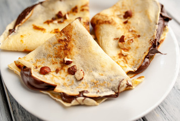 Pancakes with chocolate spread and hazelnuts,  on a white plate on a wood background