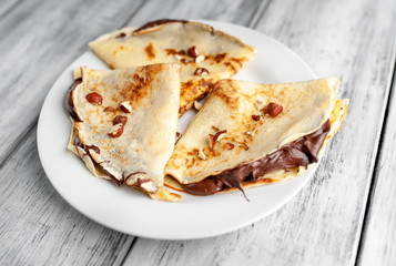 Pancakes with chocolate spread and hazelnuts,  on a white plate on a wood background