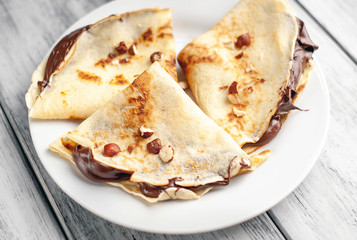 Pancakes with chocolate spread and hazelnuts,  on a white plate on a wood background