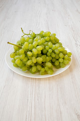 Green grape on a white plate over white wooden background, side view.