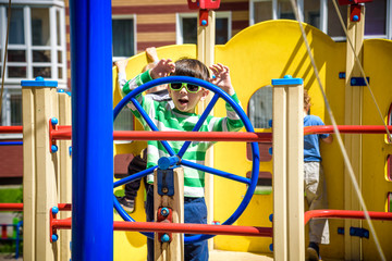 Boy as a captain or sailors play on the ship outdoors on sunny day. Kid has a lot of fun. Ship has colorful flags on wind