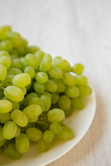 Green grape on a white plate over white wooden surface, side view. Close-up.