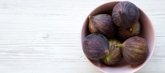 Fresh figs in a pink bowl over white wooden surface, overhead view. Top view, flat lay, from above. Copy space.