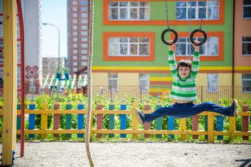 Fototapeta na wymiar Cute little kid boy enjoying climbing athletic rings on a playground. Toddler child learning to climb, having fun on warm sunny spring day. Active leisure with kids.