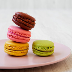 Colorful macarons on a pink plate over white wooden background, side view. Closeup.