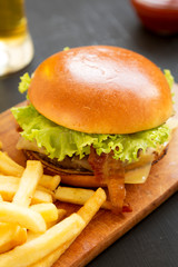 Hamburger with lettuce, cheese and bacon on a rustic wooden board, side view. Closeup.