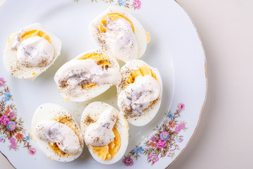 Sliced boiled eggs with mayonnaise and pepper in white plate isolated top view