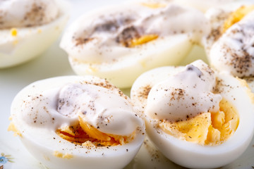 Sliced boiled eggs with mayonnaise and pepper in white plate isolated close up